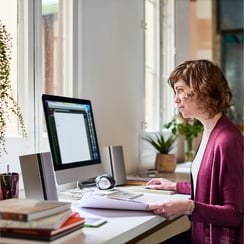 woman at sunlit desk with desktop computer and books