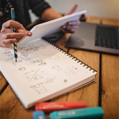 wooden desk with laptop, pens, and notebook