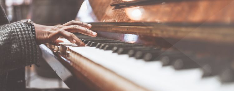 hand playing piano, piano is dark wood, hand is coming from herringbone sleeve, person of color