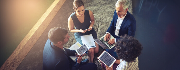 two men, two women gathered around a discussion, each with a different laptop or tablet, illustrating bring your own device
