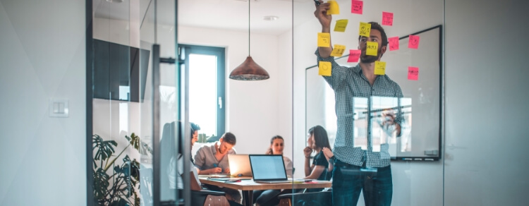 bearded man adds sticky notes to collection of them on glass wall in brainstorming session