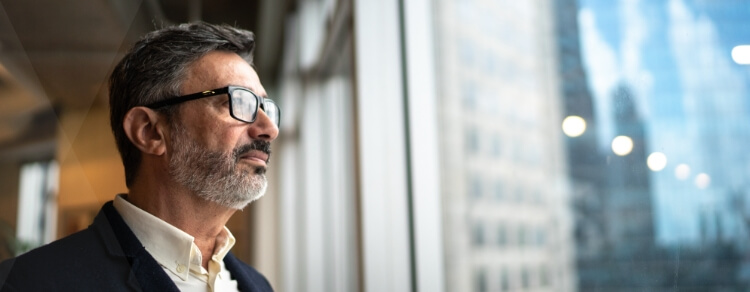 bearded man with glasses looking out office window