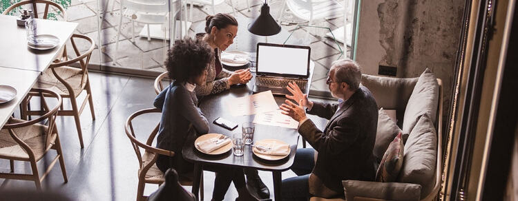 three people at a table in a restaurant, one is using gestures to explain something to the other two