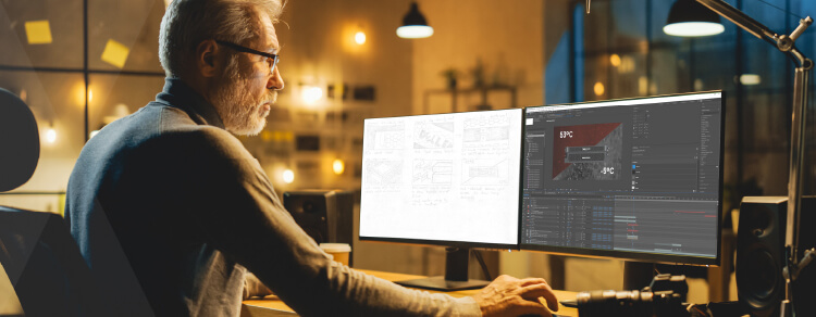 bearder man with glasses using two computer monitors