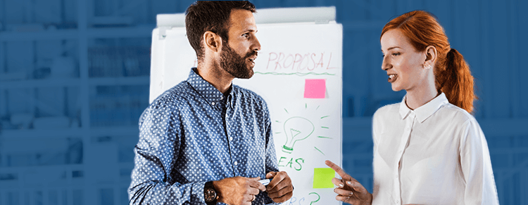 white, bearded man and white, red-haired woman talking in front of whiteboard