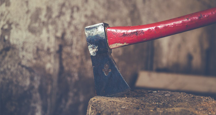 an axe blade embedded in wood as its red handle extends upward, against a rustic background