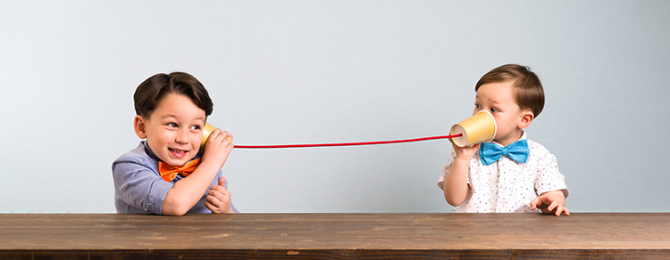 two boys using cups with string to communicate. boy on left listens happily.